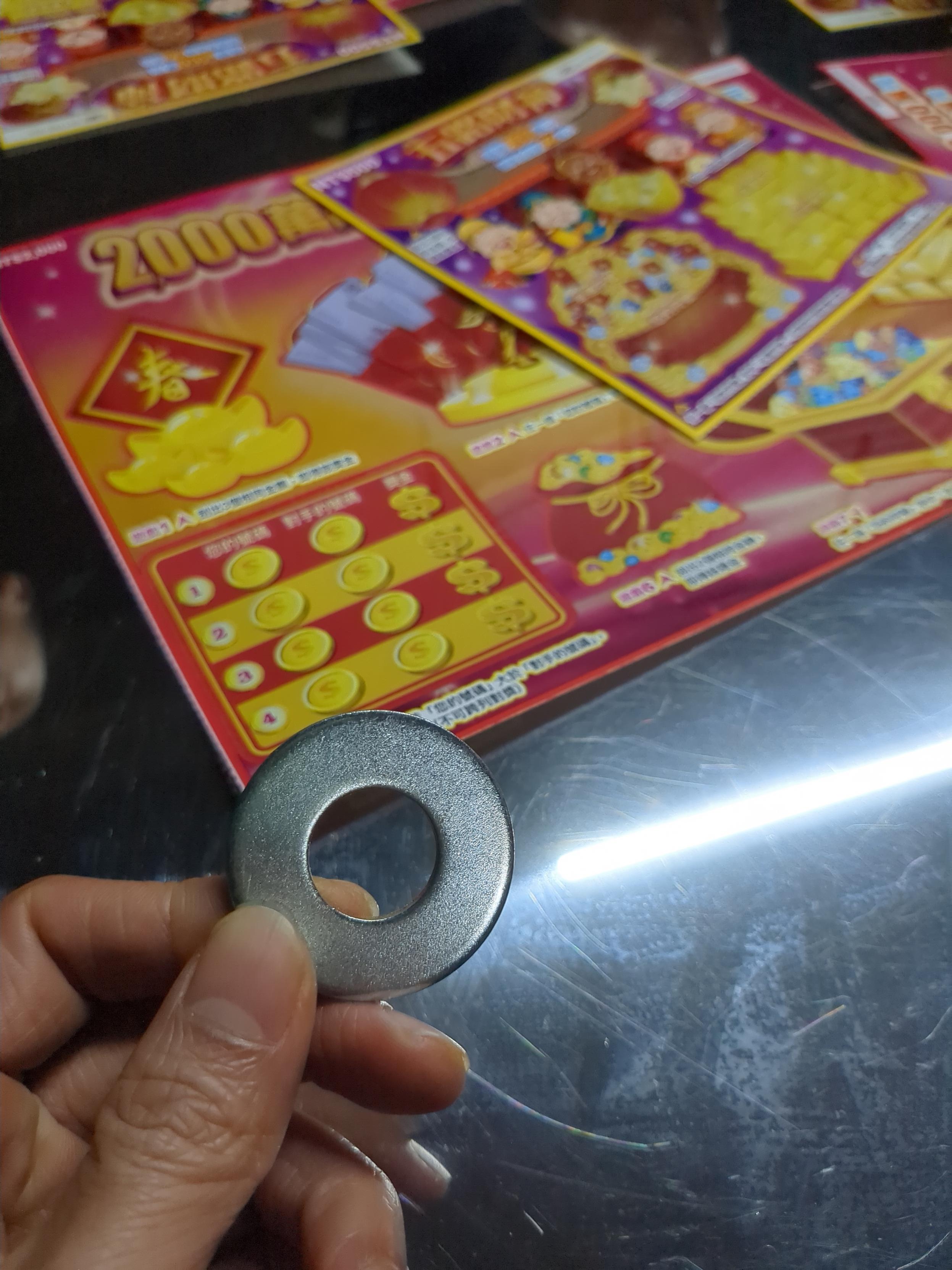 我手拿著一個螺絲墊片,桌上放著兩張刮刮樂