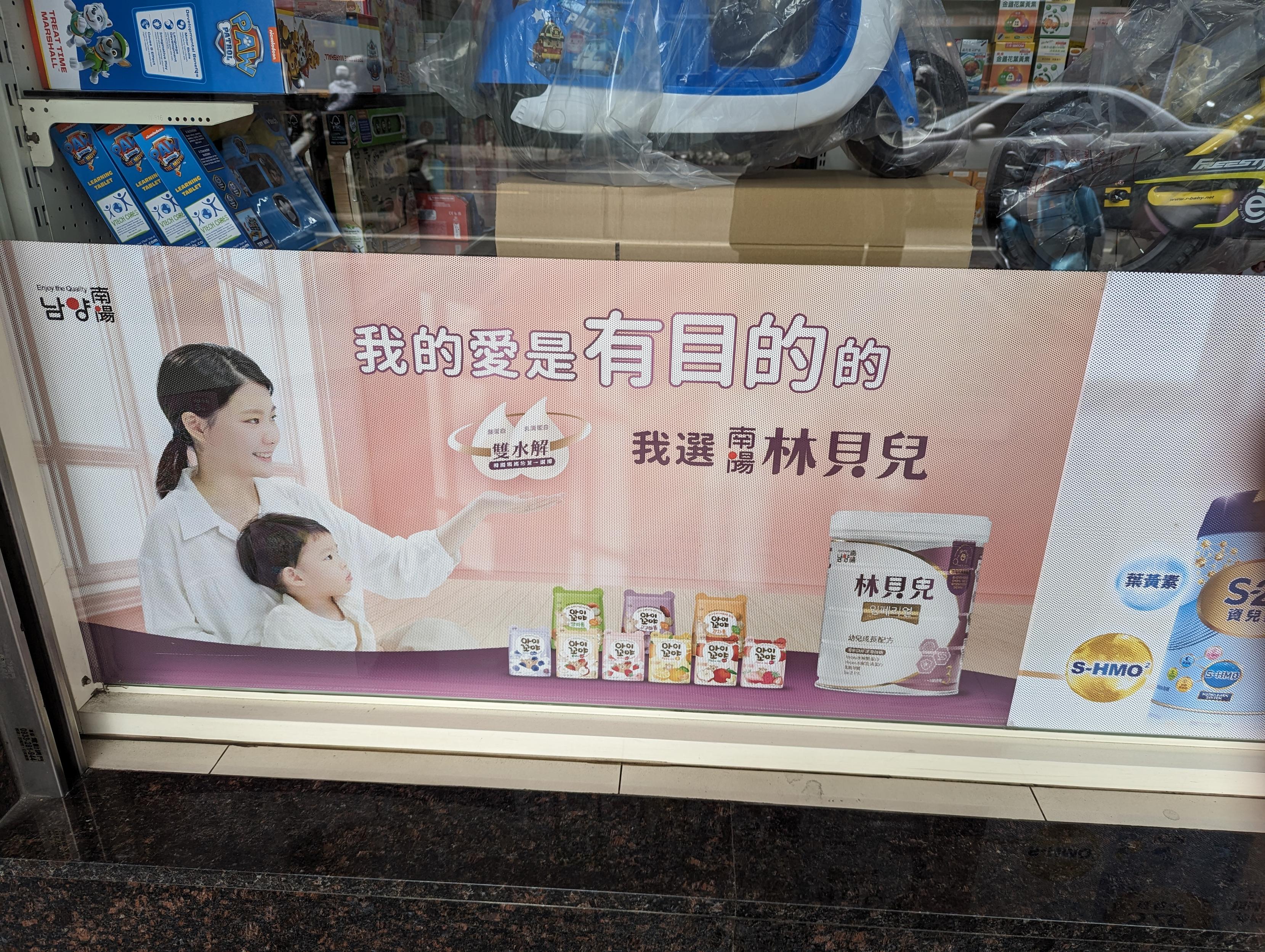 一個藥局外玻璃外牆張貼著廣告標語
商品應是奶粉
左邊有小孩依偎在媽媽懷中
媽媽面前的大標題:我的愛是 **有目的** 的